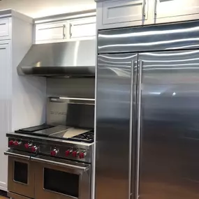 stainless steel fridge and range with hood on display with white cabinets