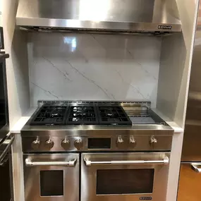 stainless steel range and hood on display with a white marble backsplash