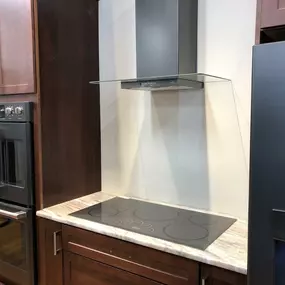 Stainless steel vent hood, cooktop, and wall ovens on display in a kitchen showroom