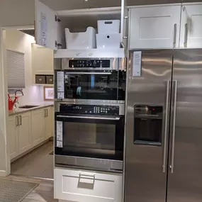 Stainless steel refrigerator and ovens on display with white cabinets