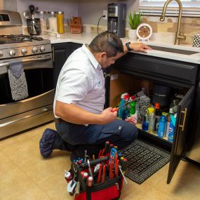 Plumber in the kitchen working on a drain cleaning service call in the Dallas Plano area.
