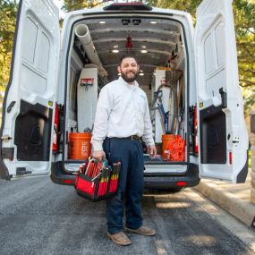 Plumber standing behind of a service van ready for a water and sewer line cleaning, repair, and replacements job in the North Dallas Irving area.