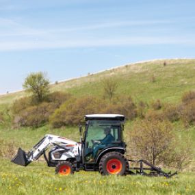 Bobcat construction tractor with three-point finish mower driving through hilly countryside.