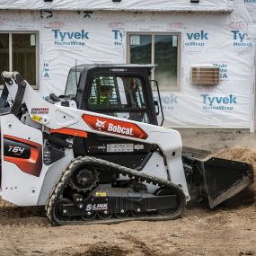 Bobcat Construction Equipment Compact Truck Loader with Bucket Attachment plowing dirt at construction site for a new building.