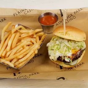 A mouthwatering Signature burger served at the Sportsbook restaurant and bar at Plainridge Park Casino in Plainville, Massachusetts. 6 oz brisket chuck patty, pickles, steamed onion, cheddar, aioli, on a potato roll.