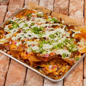 A mouthwatering platter of plus-sized nachos served at the sportsbook restaurant and bar at Plainridge Park Casino in Plainville, Massachusetts. The nachos are piled high with crispy tortilla chips topped with spicy beef, gooey queso, shredded cheddar jack cheese, diced tomatoes, onions, jalapeños, habanero crema, and fresh pico de gallo. The towering nachos are packed with Tex-Mex flavors and textures making it the perfect appetizer to enjoy at the sportsbook restaurant and bar at Plainridge Pa