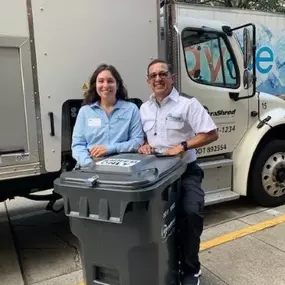 UltraShred Technologies employees Jesus and MK standing behing a gray, rolling shred bin