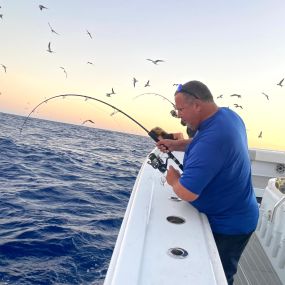 Man reeling in big fish on private boat charter in Honolulu, HI at sunset