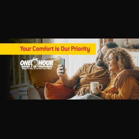 Couple sitting on a couch looking at a phone, drinking coffee, & smiling with the overlay text that says Your Comfort is Our Priority with the One Hour logo | One Hour Heating & Air Conditioning |  Proudly serving  Cedar Park, Leander, Liberty Hill, & Lago Vista, TX and surrounding areas