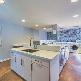 Resident Laundry Facilities with Multiple Washers and Dryers, a Tile Patterned Wall, and a sink with White Cabinetry