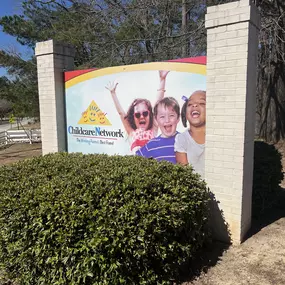 Our bright and welcoming school sign, surrounded by cheerful greenery and vibrant plants, reflects the warm, nurturing environment children experience every day inside.