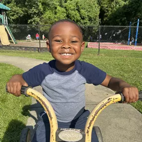 A child smiling proudly while riding a bike, enjoying the freedom and excitement of outdoor play.