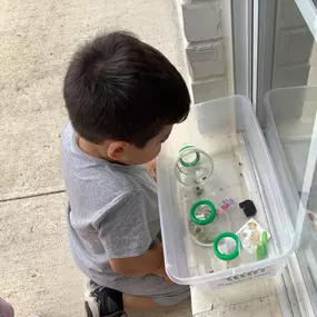 A child holds a small container with caterpillars inside, watching them closely with curiosity.