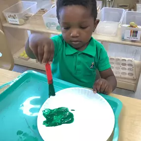 YoungA young boy is focused on painting with green paint, carefully brushing color onto his paper. boy painting with green