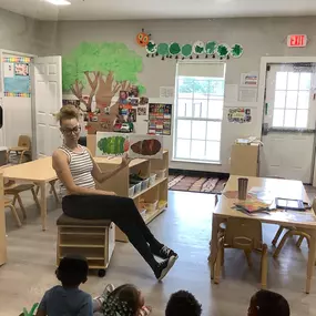 A preschool teacher is showing a group of young children a colorful poster of a caterpillar, engaging them in a lesson about insects.