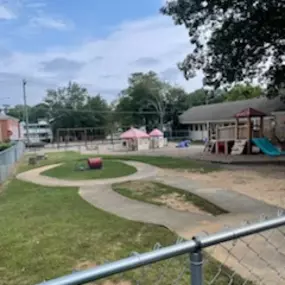 Empty playground with swings, slides, and a small playhouse in the background, surrounded by grass.