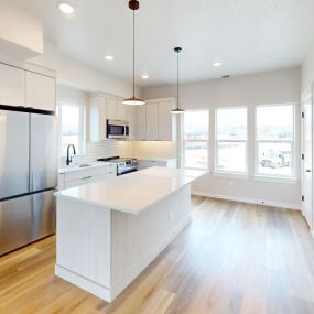 View of the kitchen from the entryway showcasing the cream wood island with quartz countertops and pendant lighting, and the fully-equipped kitchen with modern fixtures
