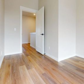 View from bedroom into living space connected by a paneled door with chic black hardware with plank flooring throughout