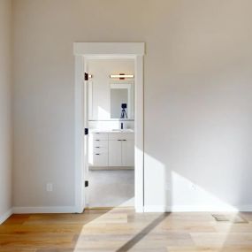 View from bedroom into the bathroom with cream built-in style vanity with two mirrors with modern vanity light fixtures