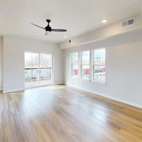 Expansive view of a living room with plank flooring, four windows, a ceiling fan, and sliding glass doors leading out onto the balcony