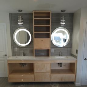 This modern style bathroom was a fun project from a few years back. It features an open, maple vanity, tile backsplash, round, lighted mirrors and some really fun lighting fixtures. Are you looking to do something unique with your bathroom remodel? Get ideas at our website.