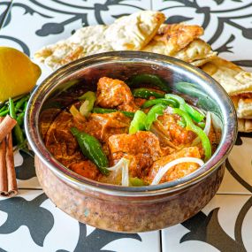 Bowl of Chicken Tikka Masala in a hammered copper serving bowl, aesthetically framed by cilantro, whole lemons, and cinnamon sticks, placed on a colorful black and white tiled surface
