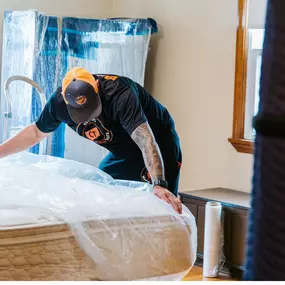 A mover carefully wraps a mattress in protective plastic.