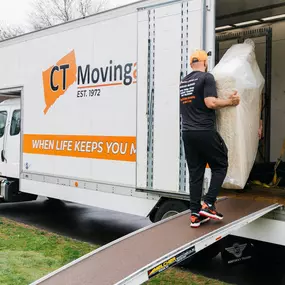 A crew member carries a mattress up the ramp into a branded CT Moving and Storage truck.