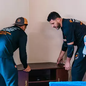 Two movers lift and reposition a piece of furniture in a customer’s home.