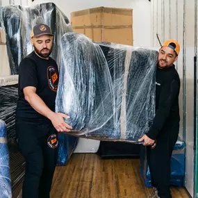 Two movers carefully handle a plastic-wrapped piece of furniture inside the truck.