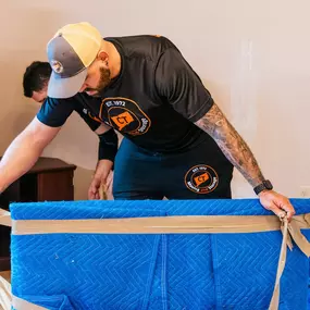 A mover ties a protective moving blanket around furniture before transport.
