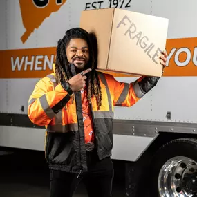 A team member proudly poses with a “FRAGILE” box in front of the truck.