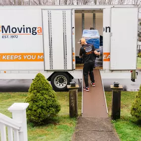 A mover walks up a truck ramp carrying a wrapped item during a home move.