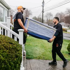 Two movers lift a plastic-wrapped sofa inside the truck, coordinating the load-in.