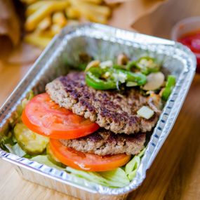 A photograph of the contents of a Five Guys burger bowl, which include two ground beef patties, tomatoes, jalapenos, lettuce and pickles.