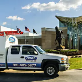 A branded Gore Heating & A/C INC company truck is parked in front of a commercial building offering commercial services. The truck is unoccupied and prominently displays the company's logo and contact information. Its clean exterior and well-maintained appearance reflect the company's professionalism and commitment to quality service