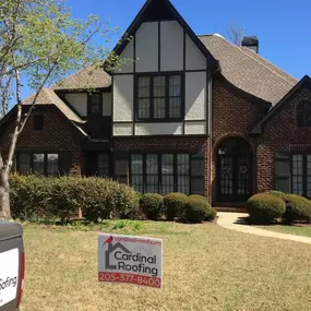 White and brown brick home featuring a Cardinal Roofing Sign in Front Yard