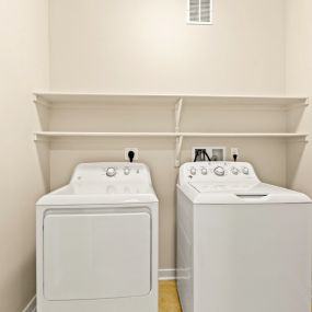 In-unit white washer and dryer set with shelving above and white walls