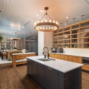 Gorgeous resident kitchen and lounge area with a patterned wood and brick wall, dark island cabinetry with gold hardware and sink, and view into the chic seating area