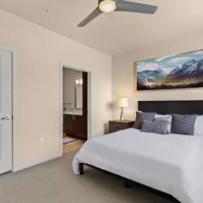 View into the cozy bedroom with a large bed, two side tables, and a ceiling fan with access into the bathroom