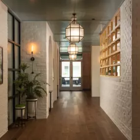 Long white brick hallway with wood flooring and geometric pendant lighting leading to resident lounge