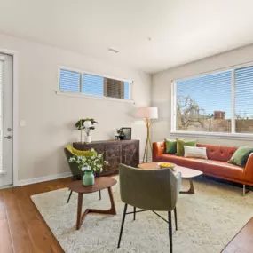 Spacious living room with a couch and chairs surrounding in natural light from the windows and door leading out to the balcony