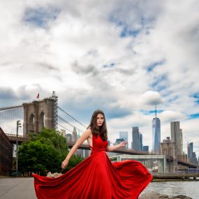Graduate posing in a red dress with Brooklyn bridge in the background