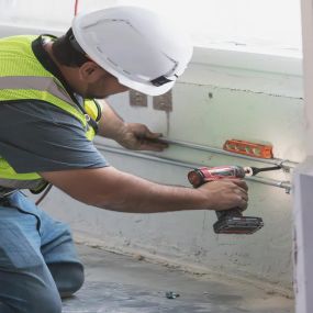 A Mappco Construction professional is diligently at work, focused on securing a component with a cordless drill on an active construction site.