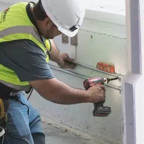 A Mappco Construction professional is diligently at work, focused on securing a component with a cordless drill on an active construction site.