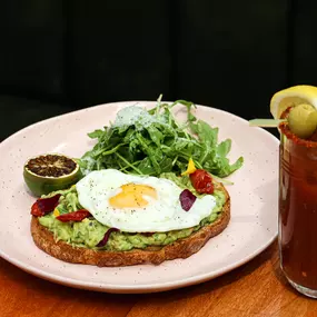 Smashed avocado toast with an egg on top and a bloody mary at Glass Ceiling Rooftop.