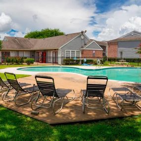 A gated outdoor community pool with lounge chairs, trees, sundeck, and grassy areas at Westbury Reserve.