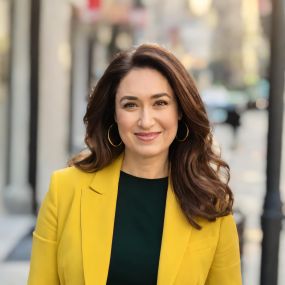 Portrait of Aisha Williams, Esq., taken on city sidewalk, wearing black blouse and yellow blazer