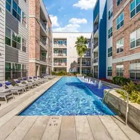 The swimming pool with chaise lounge chairs and a palm tree in front of the apartment building