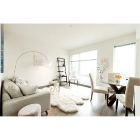 A light filled living room with large windows, a glass sliding door to the patio, filled with a white couch, white rug, and a small table of chairs